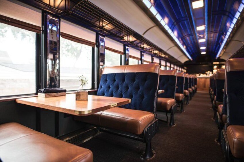 A train interior with leather seats, tables, and large windows. 2