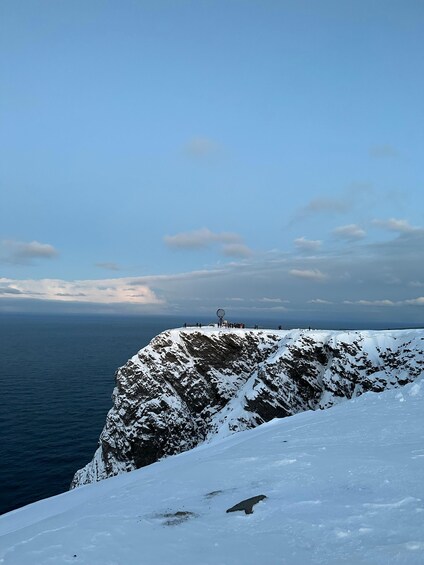 A snow-covered cliff with a clear view of the ocean and a distant horizon. 3