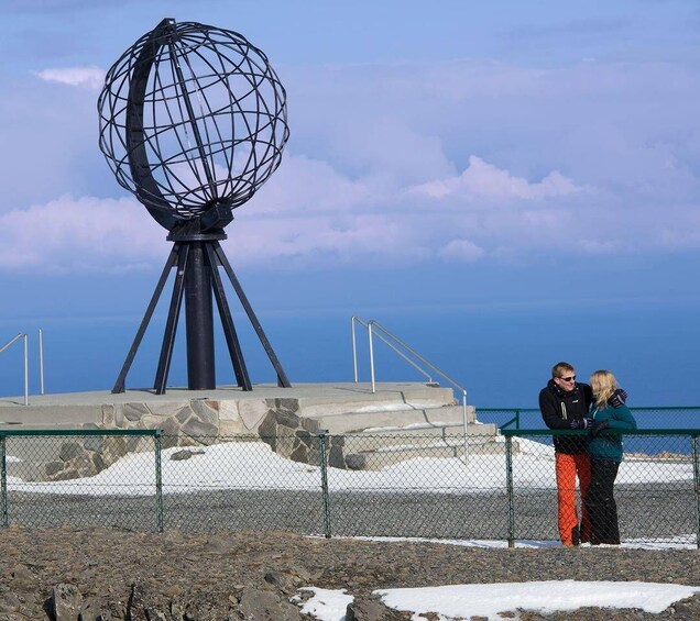 A large spherical structure with a tripod base, a fenced area with snow patches, and a clear sky. 1