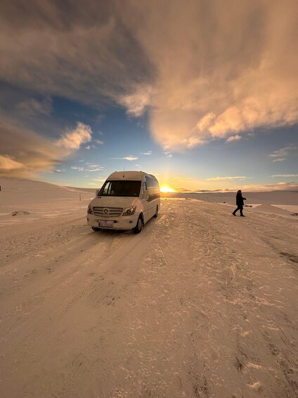 A white van on a snow-covered road with a person walking in the distance. 5