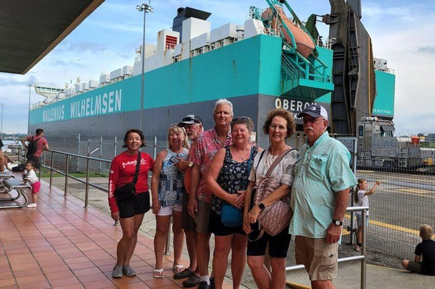A group of people standing in front of a large ship named 'WILHELM SEN' with a crane and a smaller ship in the background. 1