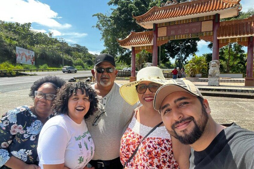 A group of people posing in front of a traditional gate with a tiled roof and stone pillars. 5