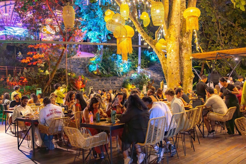 An outdoor dining area with wicker chairs and tables, surrounded by trees and decorative lights. 3