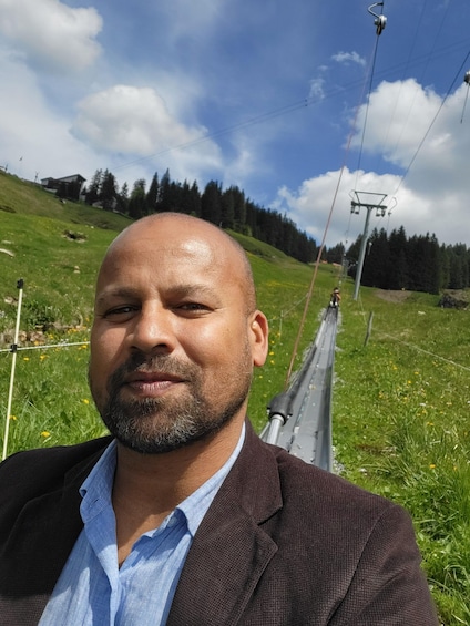 A man in a suit with a green landscape and a ski lift in the background. 1
