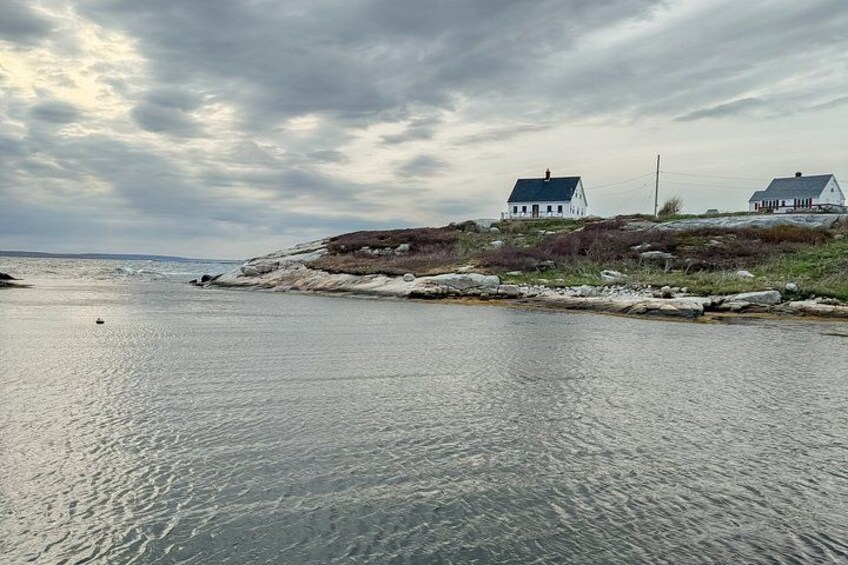 A coastal scene with two white houses on a rocky outcrop, calm water, and a cloudy sky. 2