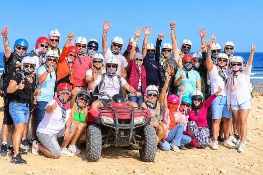 A group of people on a beach with an ATV in the center. 2