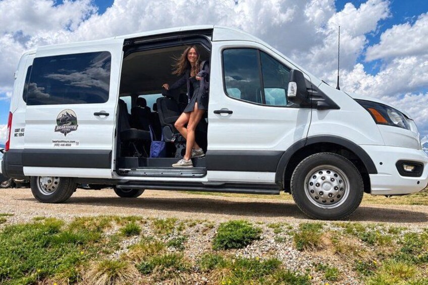 A white van with a logo on the side parked on a gravel road with grass in the foreground. 4