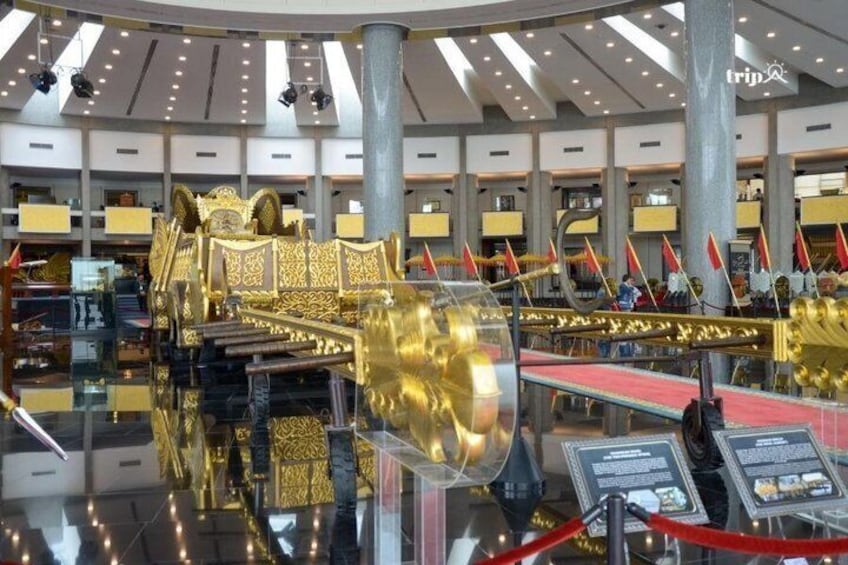 A grand golden throne with intricate designs, surrounded by flags and a reflective floor, set in a spacious, modern interior. 4