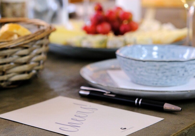 A table with a basket, a bowl, a plate, a pen, and a note with 'Cheers!' written on it. 2