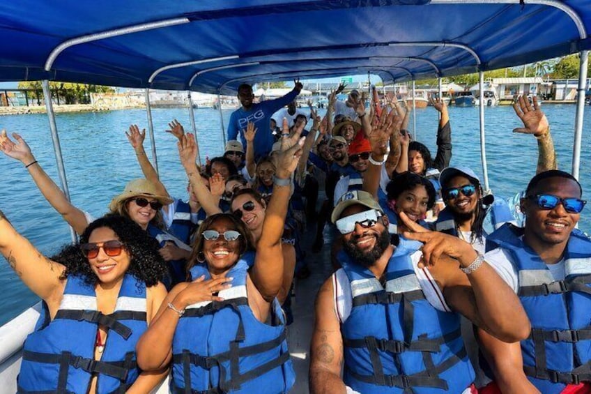 Un grupo de personas en un bote, usando chalecos salvavidas azules, con agua y un muelle al fondo. 5