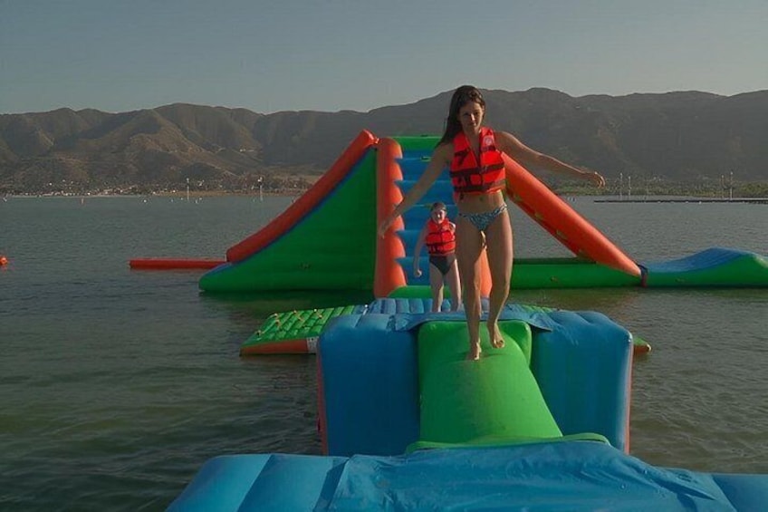 A person on a water slide with inflatable structures, a body of water, and mountains in the background. 2