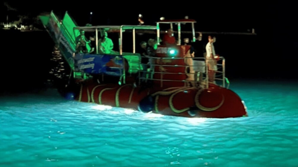 A brightly lit boat with passengers, moving through turquoise water. 4