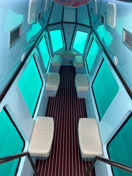 A boat's interior with teal-colored windows, a central aisle, and white cushioned seating. 3
