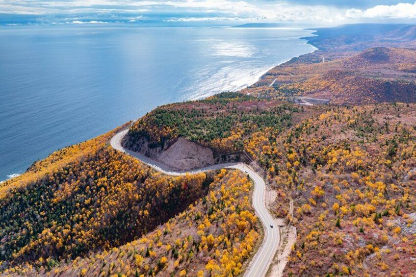 A coastal road winding through autumn-colored forest, overlooking a vast ocean and distant land. 3