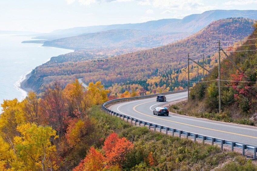 A winding road with autumn foliage, a coastal view, and a mountainous backdrop. 4