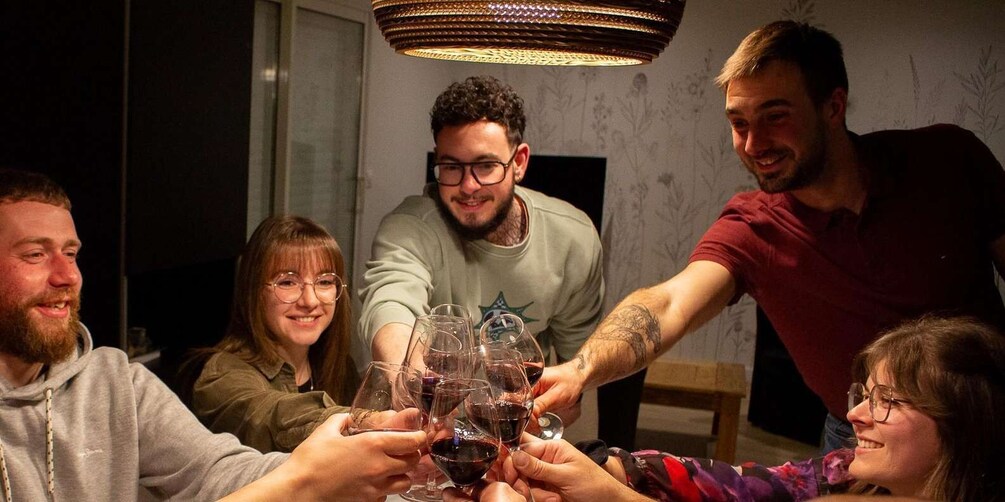 A group of people toasting with wine glasses in a dimly lit room with a patterned wallpaper and a hanging light fixture. 1