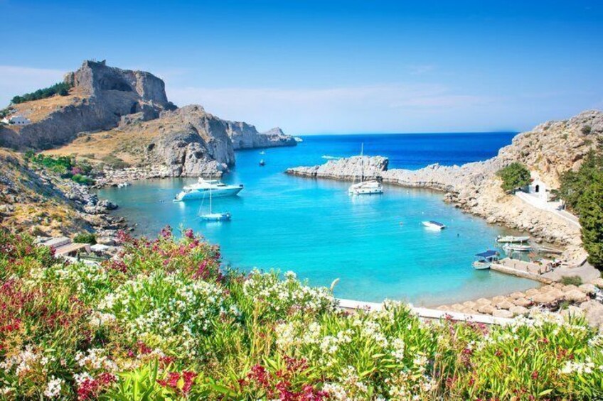 A coastal landscape with boats, rocky cliffs, and a clear blue sea. 2