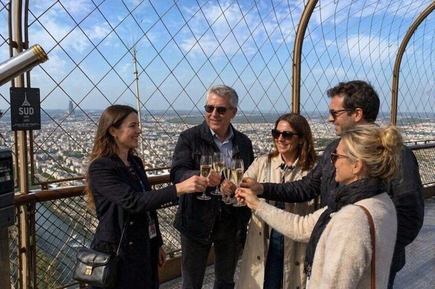 A group of people toasting with champagne glasses on a high observation deck with a cityscape in the background. 1