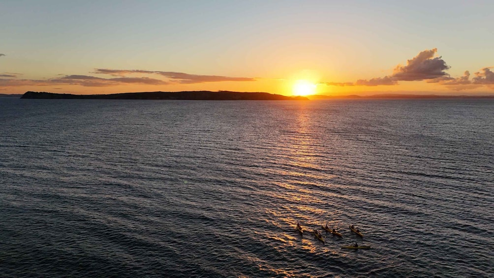 A sunset over a calm sea with a distant landmass. 1