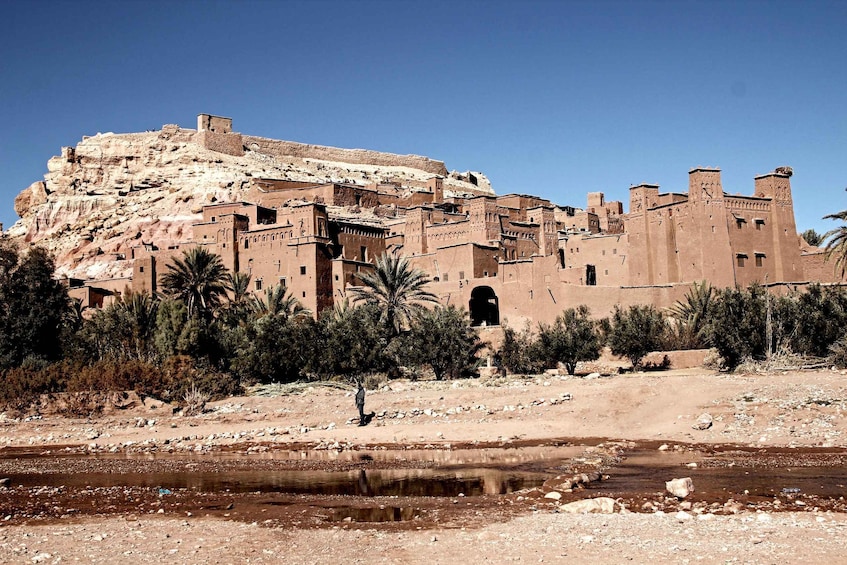 A historic fortress with a large wall and towers, situated on a hill with sparse vegetation. 1