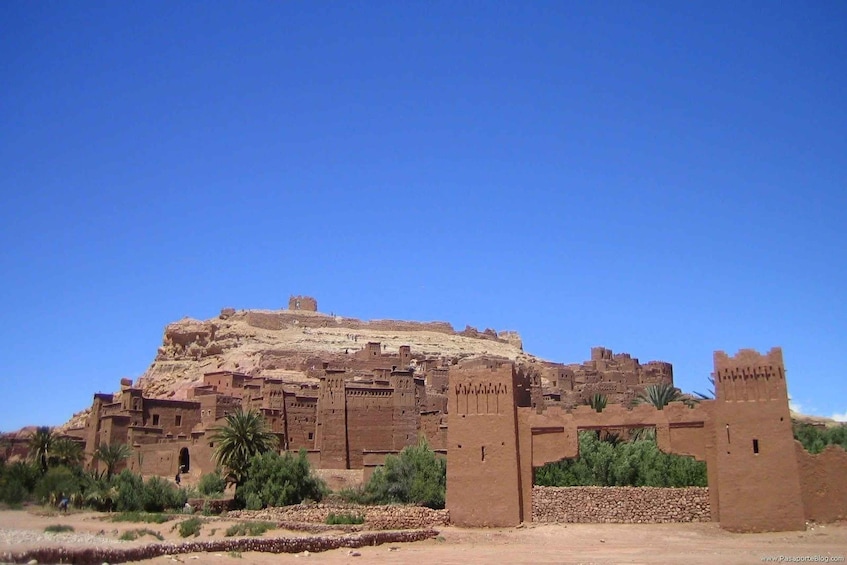 A large adobe fort with multiple towers and a surrounding wall, set against a clear blue sky. 3