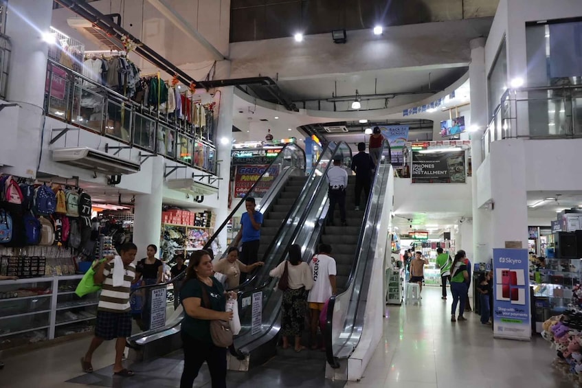 A shopping mall with an escalator, various stores, and shoppers. 5