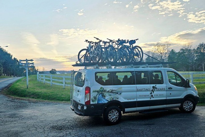 Un fourgon blanc, avec des vélos fixés sur le toit, est garé sur une route de campagne. 4