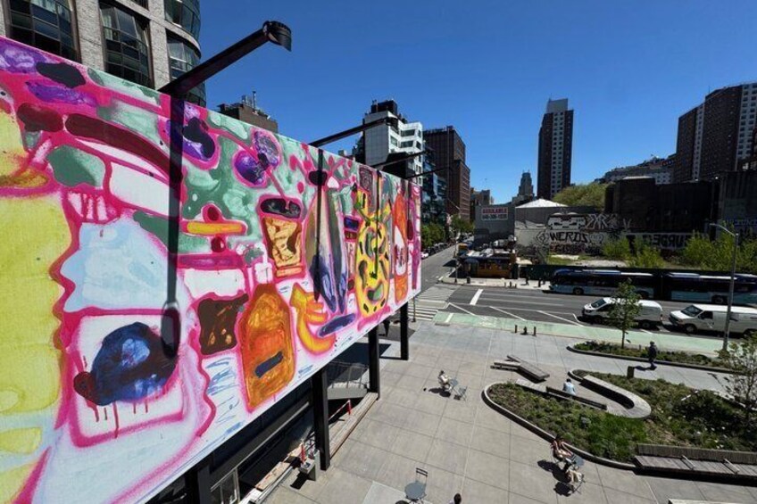 Un mural colorido en un edificio, una calle urbana con un autobús, y edificios modernos al fondo. 3