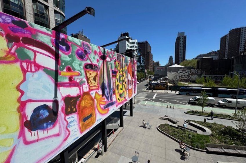 En färgglad väggmålning på en byggnad, en stadsgata med en buss och moderna byggnader i bakgrunden. 3