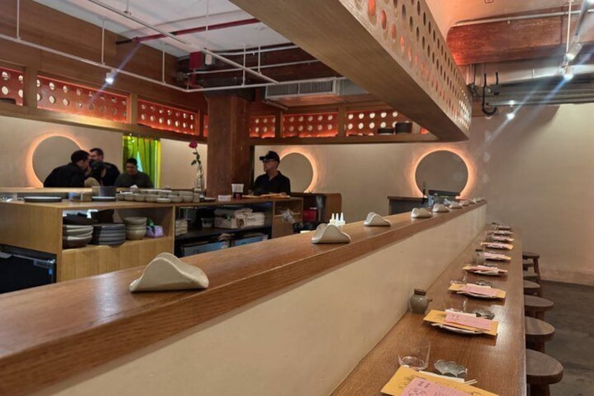 En restaurang med en inredning som präglas av en lång trädisk, runda bord och en modern takdesign. 4