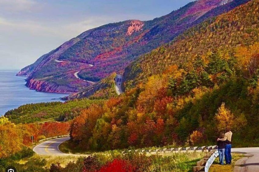 Una strada tortuosa attraversa una zona montuosa con foglie autunnali, con vista su un corpo d'acqua. 2