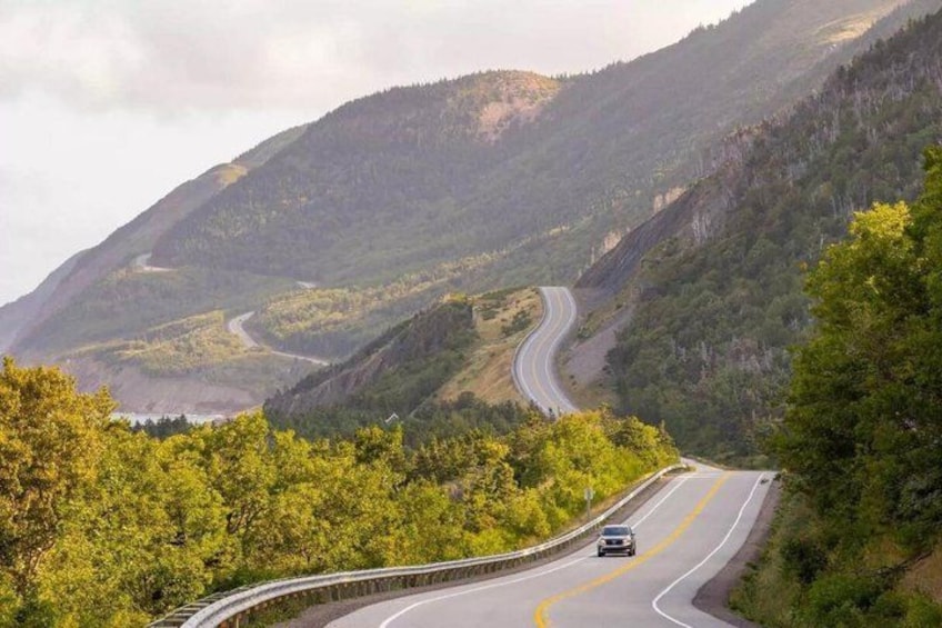 Una carretera sinuosa de montaña con un coche, rodeada de densos bosques y colinas verdes. 3