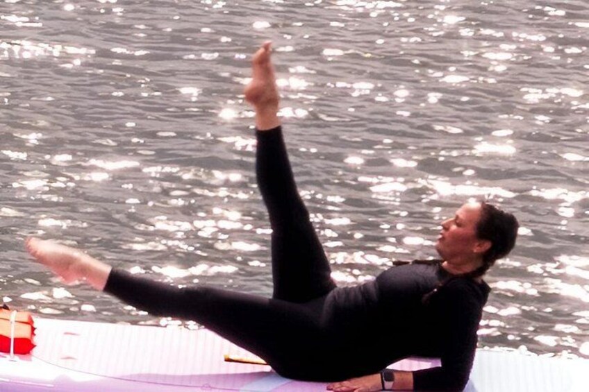 Una persona con traje de neopreno negro haciendo una postura de yoga sobre una esterilla junto al agua. 3