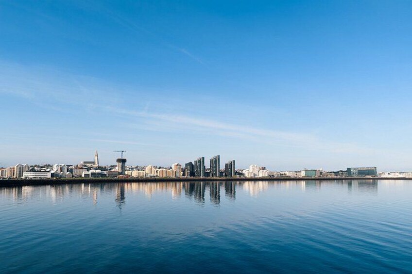 A calm waterfront cityscape with a clear sky, reflecting buildings and a tower. 2