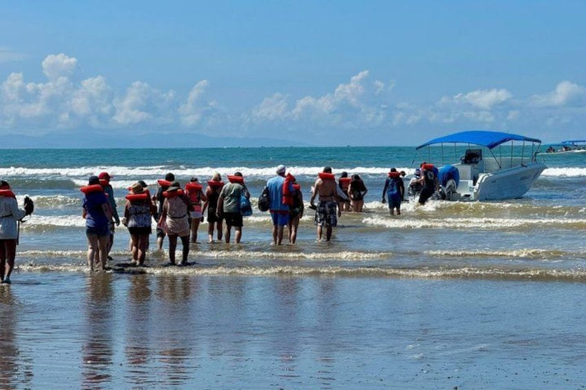 A group of people walking along the beach, a boat in the water, and the ocean in the background. 3