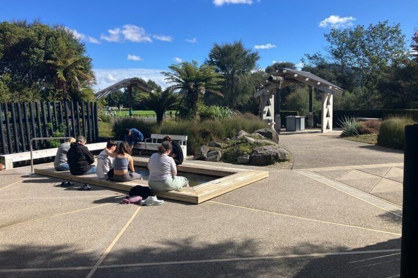 A group of people sitting on benches in a park with a pergola and a gazebo in the background. 5