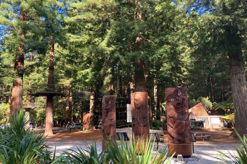 A forested area with large trees, a stone sculpture, and a bench. 2