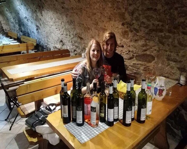 A rustic cellar with wooden benches and a table laden with wine bottles. 5