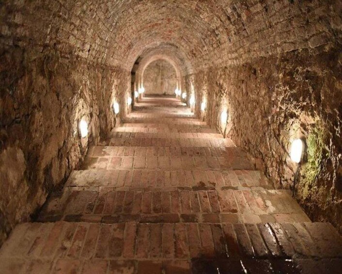 A stone tunnel with arched ceilings and brick flooring. 4