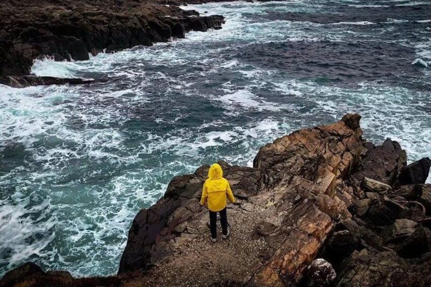 Una persona con una chaqueta amarilla de pie sobre un promontorio rocoso junto al mar. 2
