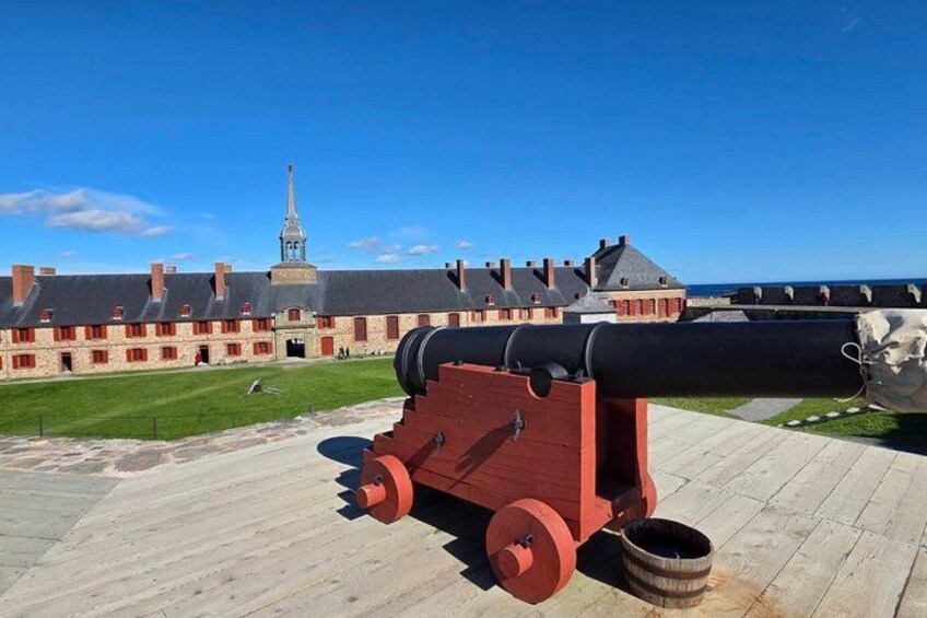 A large cannon on a platform, a historic building with a tower, and a clear blue sky. 2