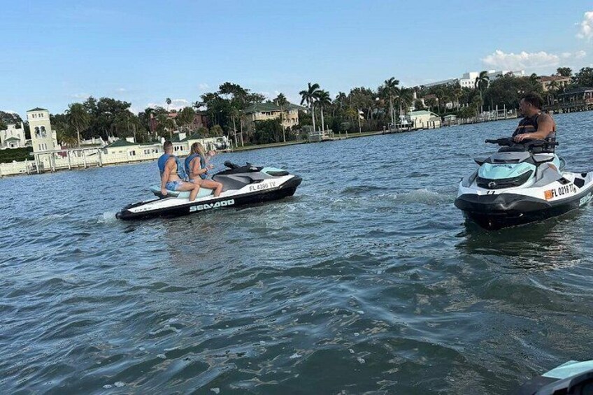 Two watercraft on a calm body of water with a clear sky and a distant shoreline with buildings and palm trees. 2