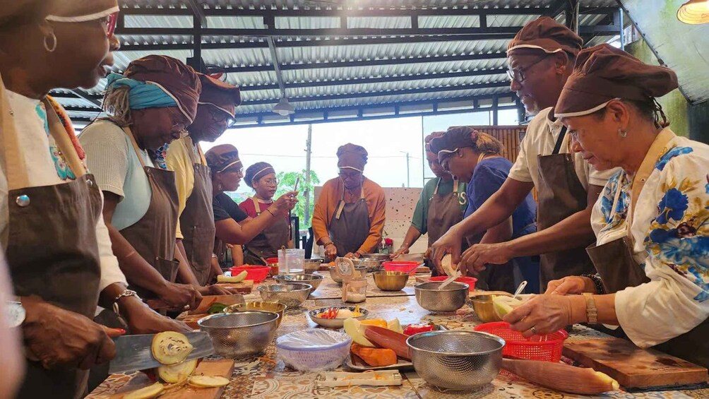 A group of people preparing food in a covered outdoor area with metal tables and various cooking utensils. 5