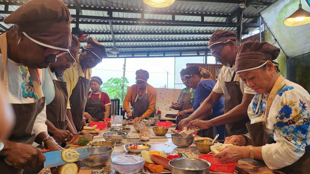 A group of people preparing food in a covered outdoor area with a metal roof and tables. 2
