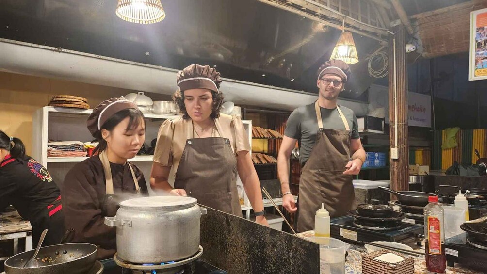 A kitchen with chefs preparing food, cooking equipment, and ingredients. 3