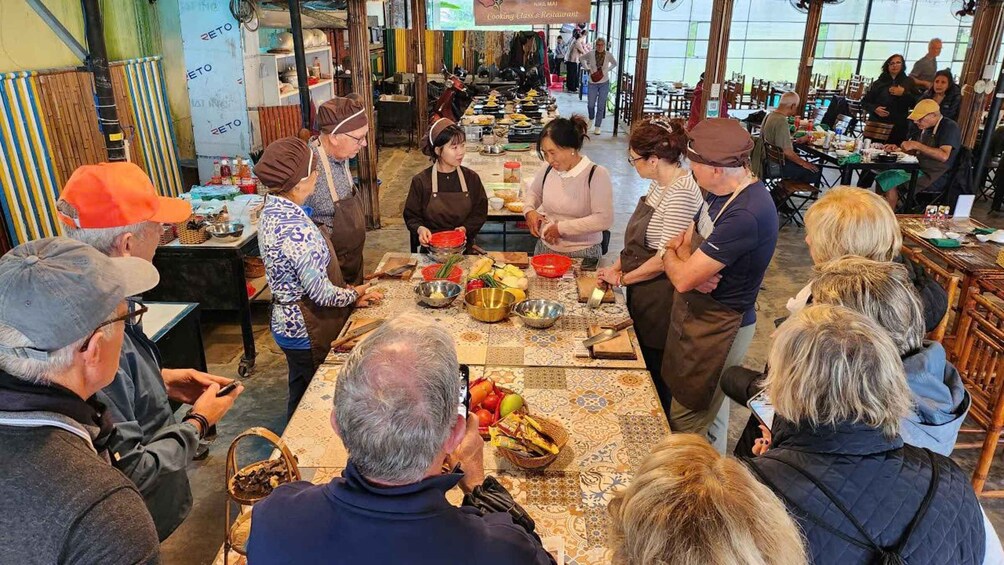 A group of people engaged in a cooking class in a spacious, well-lit room with tables set up for food preparation. 4