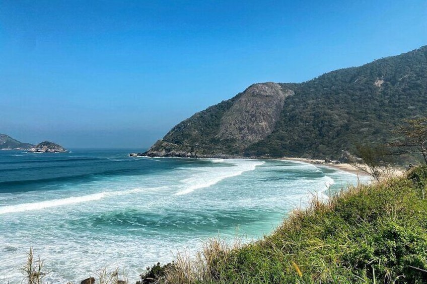 A coastal landscape with clear blue waters, a sandy beach, and a mountainous backdrop. 5