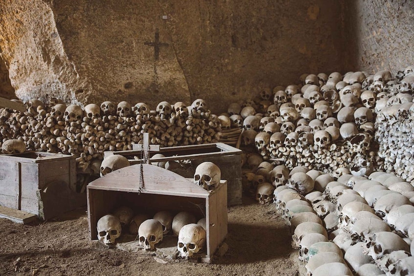 A room filled with numerous skulls, some in wooden boxes, and a cross on the wall. 2