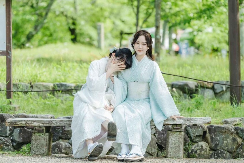 Two people in traditional attire sitting on a stone bench in a park. 2