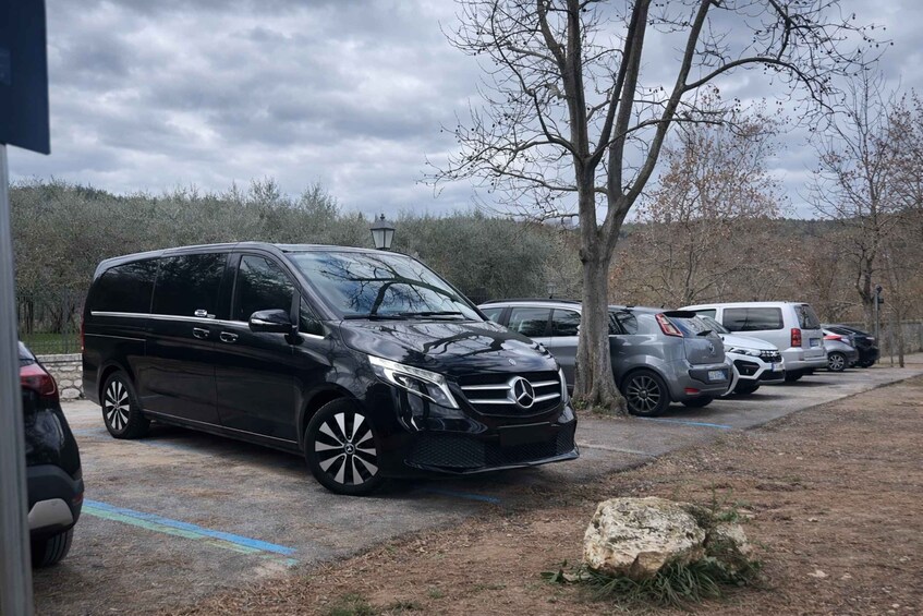 Musta Mercedes-Benz-merkkinen maasturi oli pysäköitynä parkkipaikalle, jossa oli myös muita ajoneuvoja ja puita. Taustalla näkyi pilvinen taivas. 2